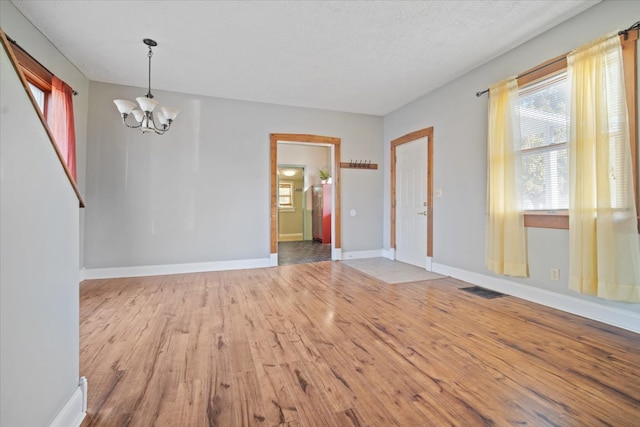 empty room featuring wood-type flooring, an inviting chandelier, and a textured ceiling