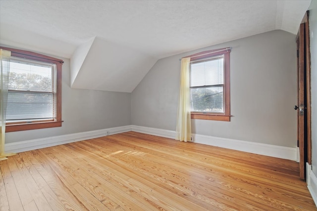 additional living space featuring light wood-type flooring, a wealth of natural light, and vaulted ceiling