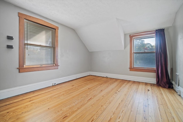 additional living space with a textured ceiling, lofted ceiling, and light hardwood / wood-style flooring