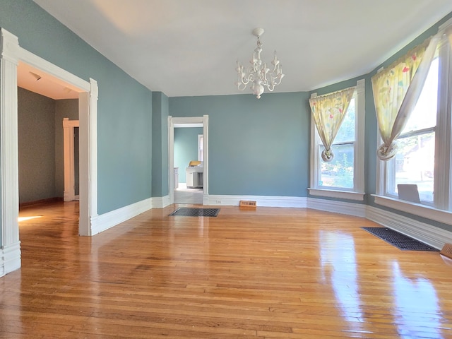 spare room featuring an inviting chandelier and light hardwood / wood-style floors