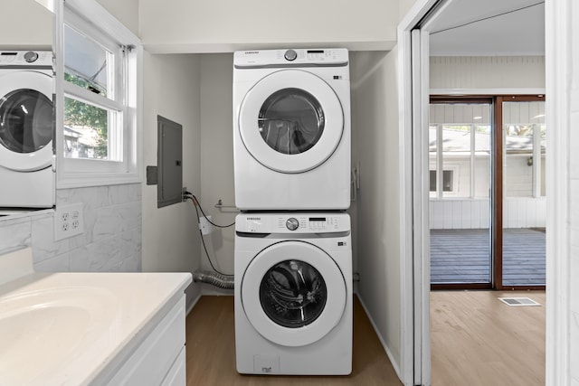 washroom with electric panel, stacked washing maching and dryer, and light hardwood / wood-style floors