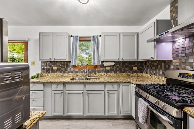 kitchen featuring wall chimney range hood, a healthy amount of sunlight, sink, and stainless steel gas stove