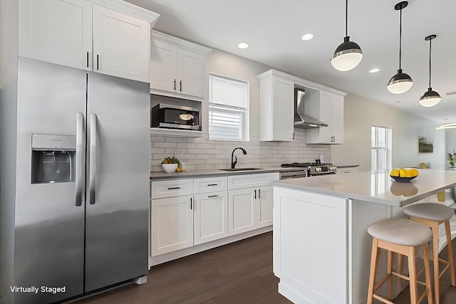 kitchen featuring a sink, a kitchen breakfast bar, stainless steel appliances, white cabinets, and wall chimney range hood