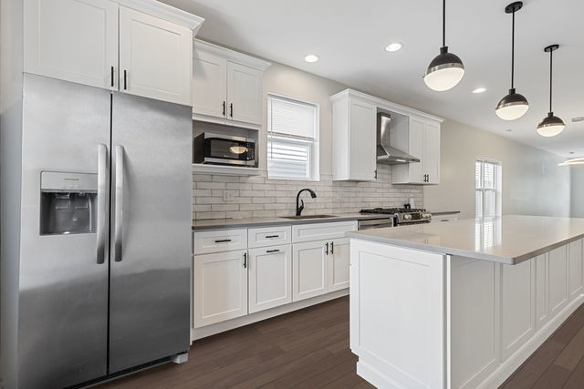 kitchen featuring hanging light fixtures, wall chimney range hood, white cabinets, and appliances with stainless steel finishes