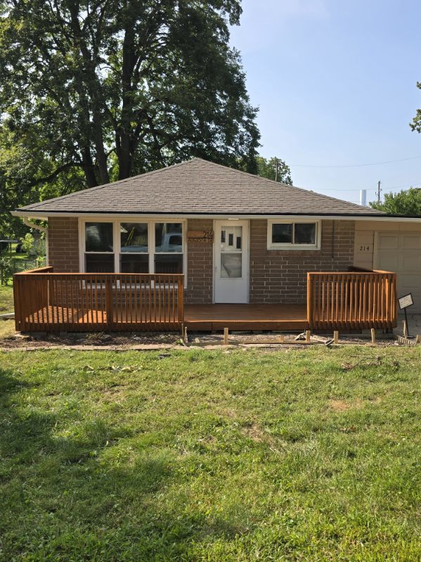 back of property featuring a garage, a lawn, and a wooden deck