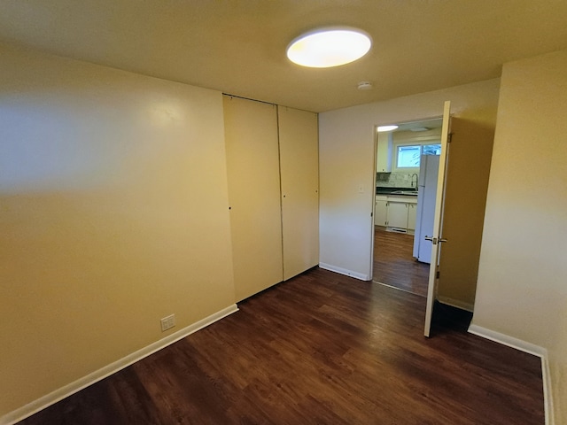 unfurnished bedroom featuring white refrigerator, a closet, sink, and dark hardwood / wood-style flooring