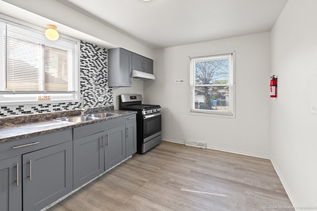 kitchen featuring gray cabinetry, stainless steel range with gas stovetop, sink, light hardwood / wood-style flooring, and backsplash