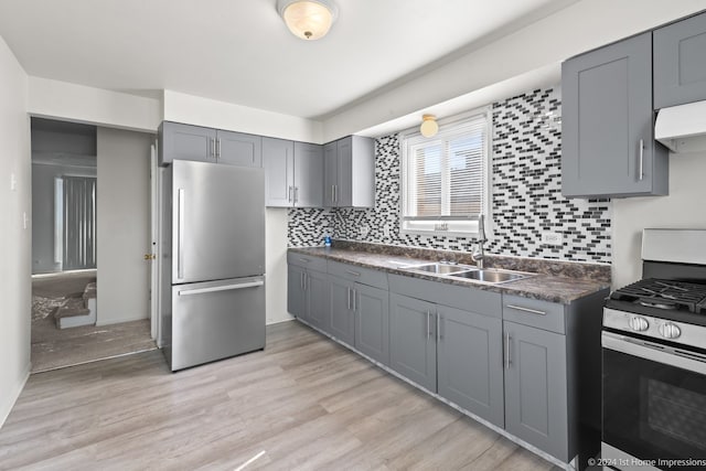 kitchen with light wood-type flooring, stainless steel refrigerator, sink, gray cabinets, and gas range oven