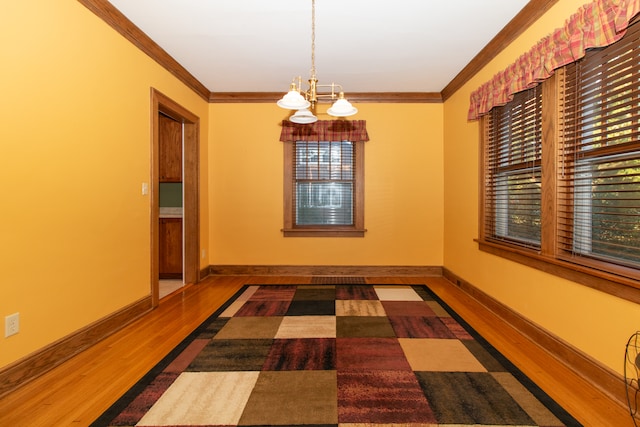 unfurnished dining area featuring wood-type flooring, a notable chandelier, and ornamental molding