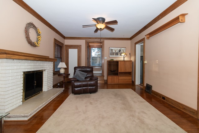 living room with a brick fireplace, crown molding, ceiling fan, and dark hardwood / wood-style floors