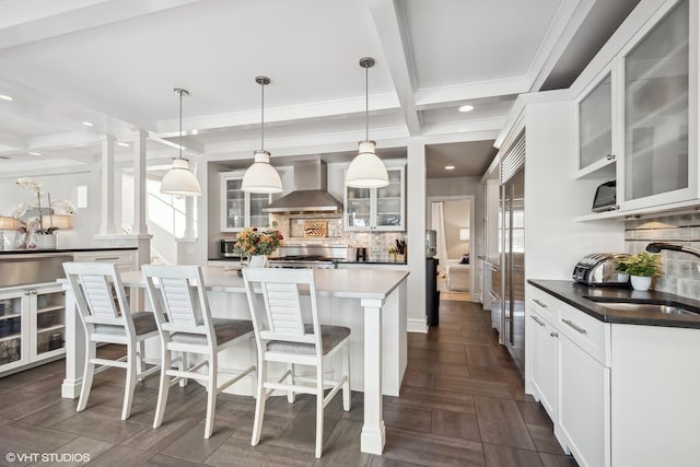 kitchen featuring sink, decorative columns, white cabinets, decorative light fixtures, and wall chimney exhaust hood