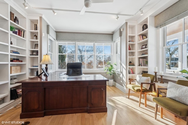 home office featuring built in shelves, ceiling fan, track lighting, and light hardwood / wood-style flooring