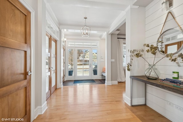 foyer entrance with an inviting chandelier, crown molding, and light wood-type flooring