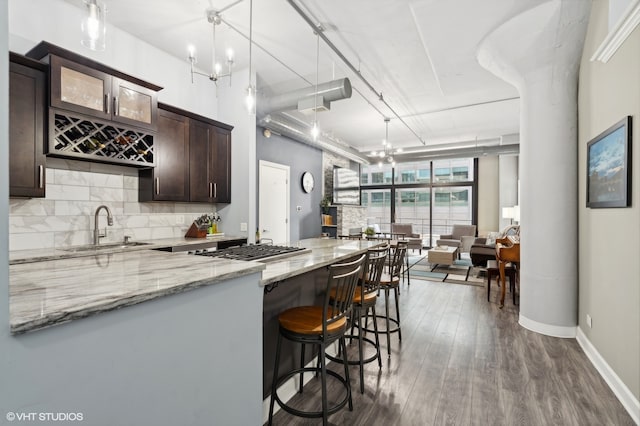 kitchen featuring sink, light stone counters, hanging light fixtures, dark brown cabinets, and dark hardwood / wood-style flooring