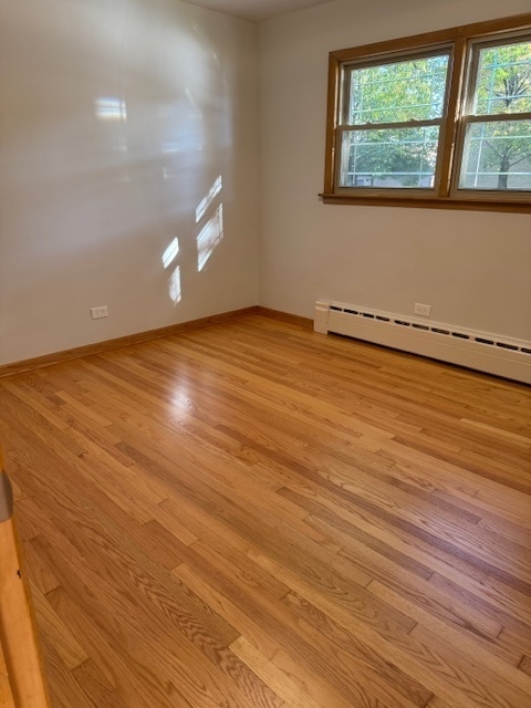 unfurnished room featuring baseboard heating and light hardwood / wood-style flooring