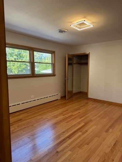 unfurnished bedroom with a closet, light hardwood / wood-style floors, and a baseboard radiator