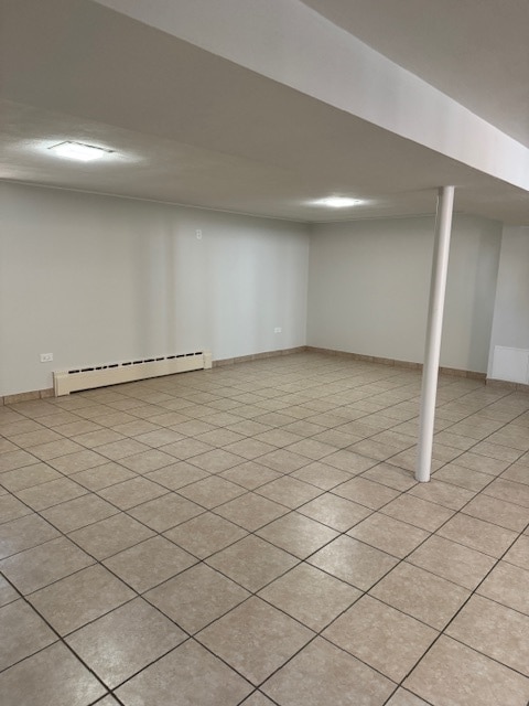 basement with light tile patterned flooring and a baseboard heating unit