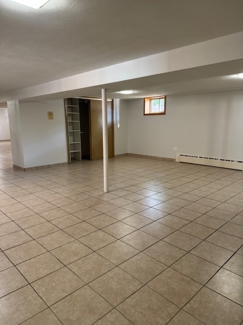 basement featuring light tile patterned flooring and a baseboard radiator