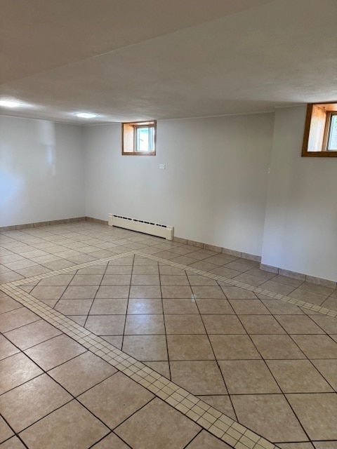 basement with a wealth of natural light, a baseboard radiator, and light tile patterned floors