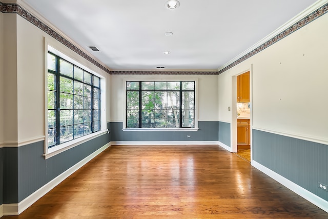 empty room with ornamental molding, wood walls, and wood-type flooring