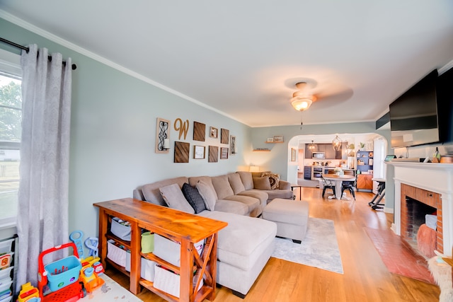 living room featuring a brick fireplace, ornamental molding, light wood-type flooring, and ceiling fan