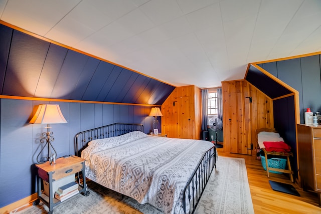 bedroom featuring lofted ceiling, wood walls, and hardwood / wood-style floors