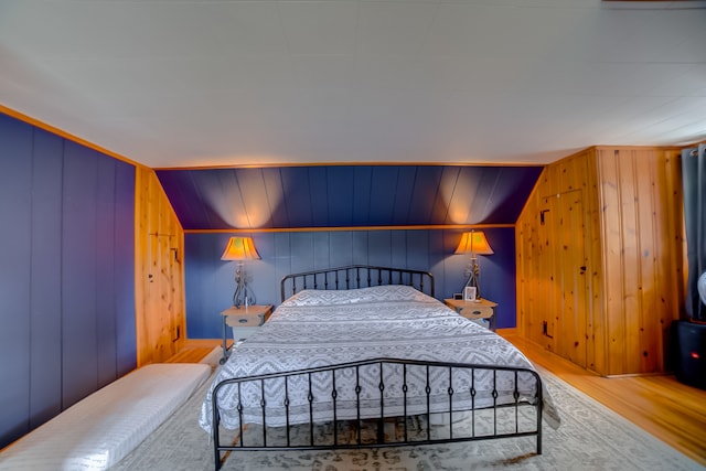 bedroom with lofted ceiling, wood-type flooring, and wooden walls