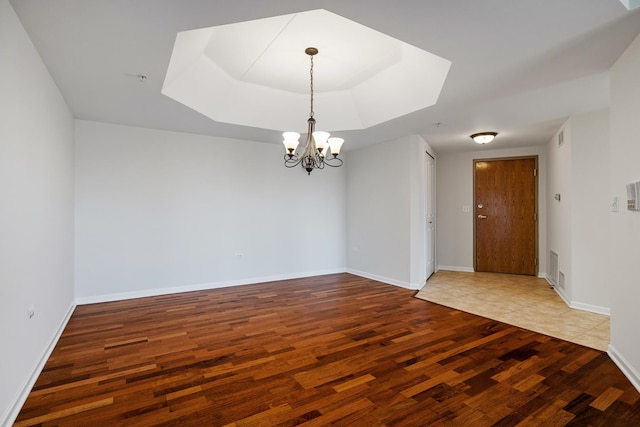 unfurnished room featuring wood finished floors, visible vents, baseboards, a raised ceiling, and a chandelier