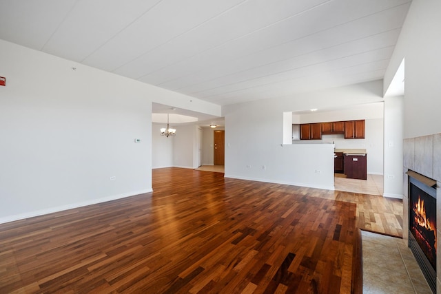 unfurnished living room with a notable chandelier, a fireplace, baseboards, and wood finished floors