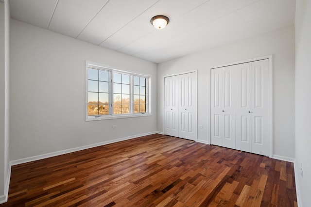 unfurnished bedroom with baseboards, two closets, and wood finished floors