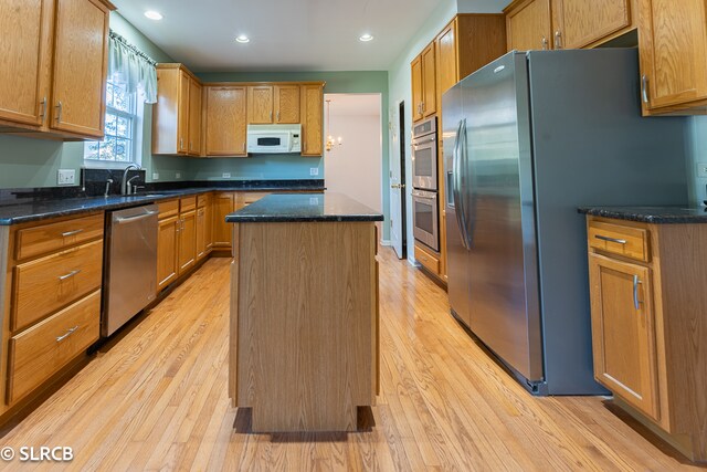 kitchen with light hardwood / wood-style floors, dark stone counters, a kitchen island, sink, and appliances with stainless steel finishes