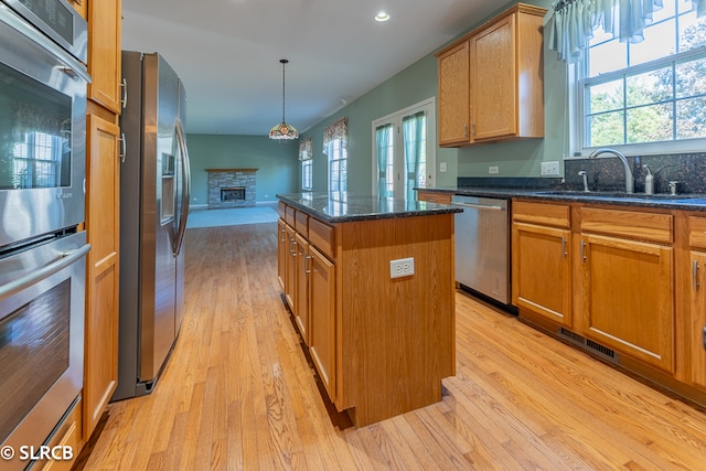 kitchen with a kitchen island, light hardwood / wood-style flooring, sink, a stone fireplace, and appliances with stainless steel finishes