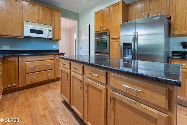 kitchen with dark stone countertops, appliances with stainless steel finishes, and light wood-type flooring