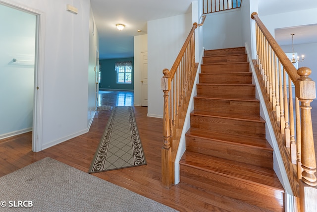 stairs with hardwood / wood-style floors and an inviting chandelier