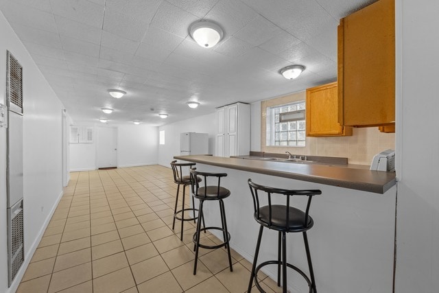 kitchen featuring white refrigerator, light tile patterned floors, sink, kitchen peninsula, and a kitchen bar