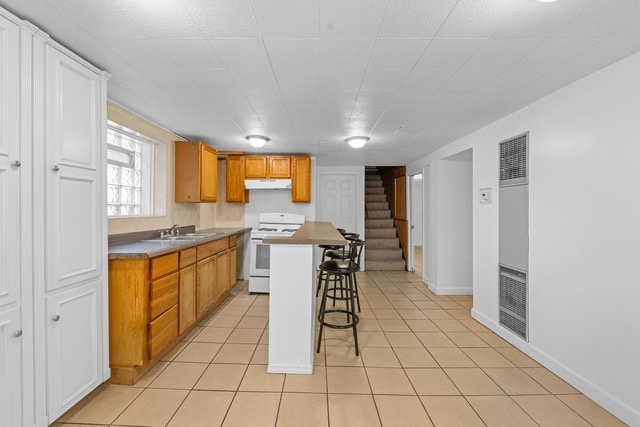 kitchen with light tile patterned flooring, sink, a kitchen island, white range oven, and a breakfast bar area