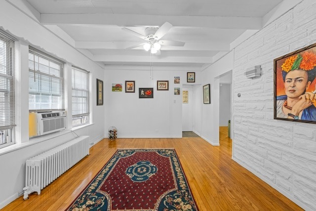 interior space with ceiling fan, beam ceiling, radiator heating unit, and light hardwood / wood-style flooring