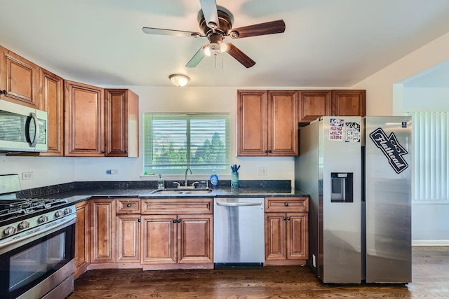 kitchen with sink, dark hardwood / wood-style floors, dark stone counters, and appliances with stainless steel finishes