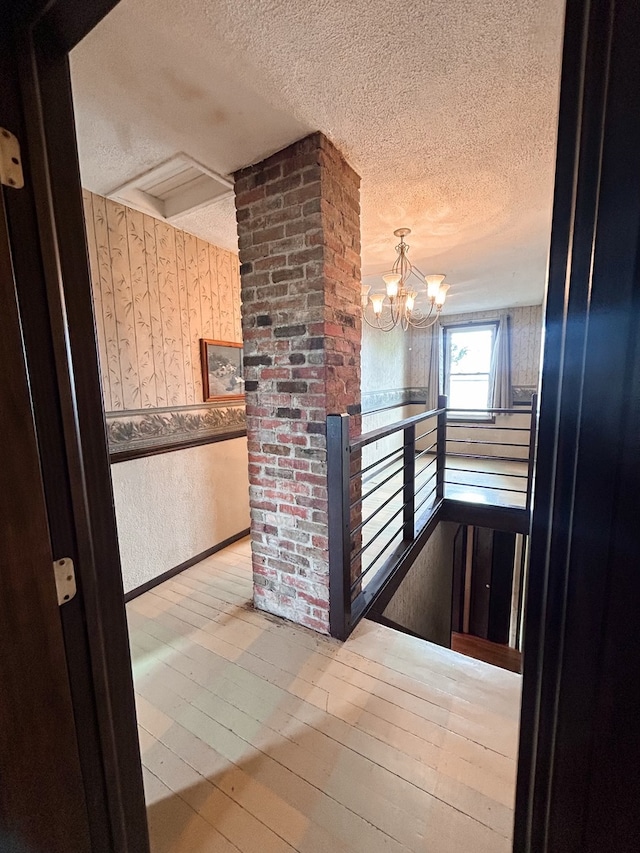 hallway featuring an inviting chandelier, light wood-type flooring, and a textured ceiling