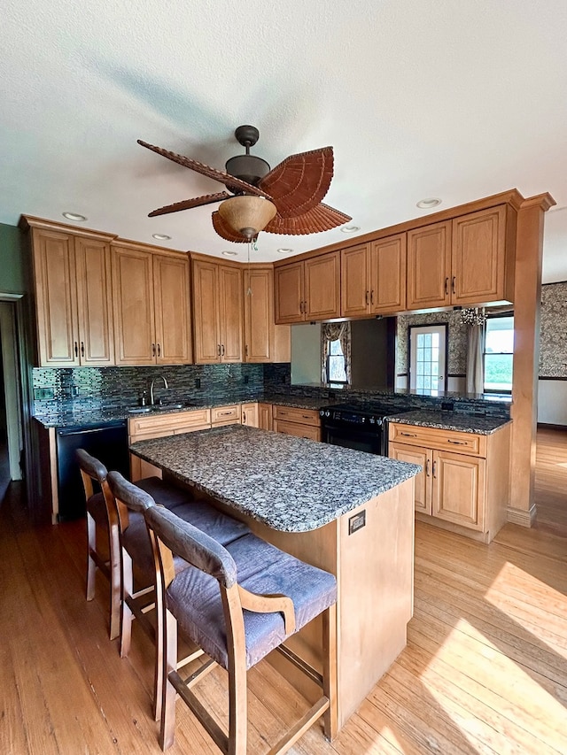 kitchen featuring ceiling fan, a breakfast bar, light hardwood / wood-style floors, and black appliances