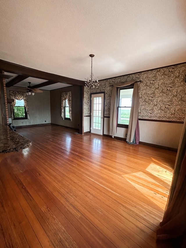 unfurnished dining area featuring ceiling fan with notable chandelier, hardwood / wood-style flooring, beam ceiling, and a textured ceiling