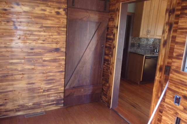 interior details with black dishwasher, wooden walls, backsplash, and hardwood / wood-style floors