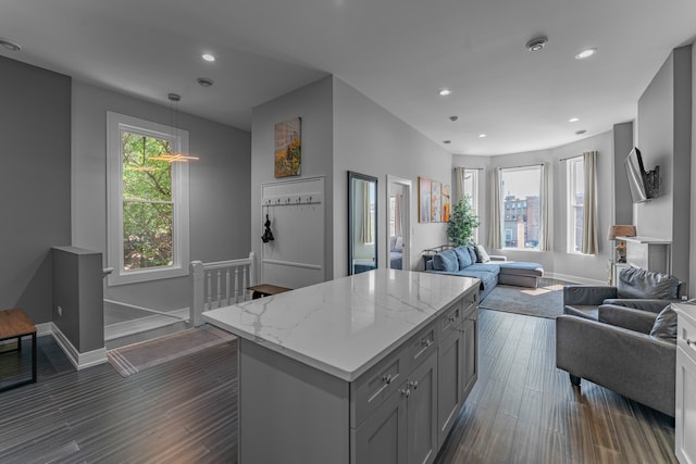 kitchen with gray cabinets, pendant lighting, dark hardwood / wood-style flooring, light stone counters, and a center island