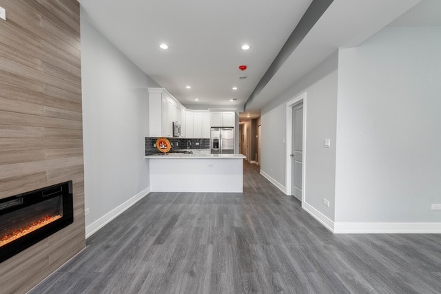 kitchen with kitchen peninsula, white cabinetry, appliances with stainless steel finishes, dark hardwood / wood-style floors, and a tile fireplace