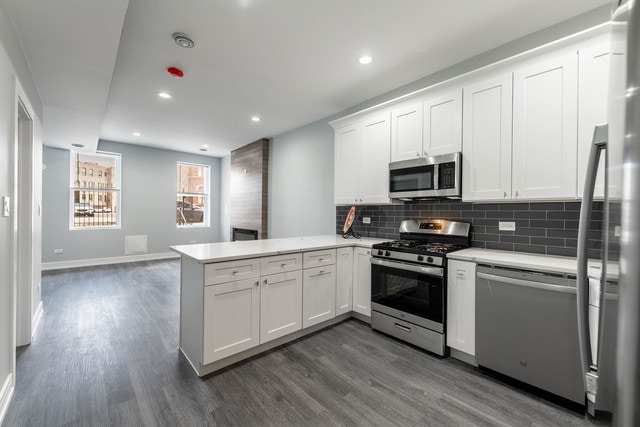 kitchen with appliances with stainless steel finishes, kitchen peninsula, dark hardwood / wood-style floors, and white cabinets