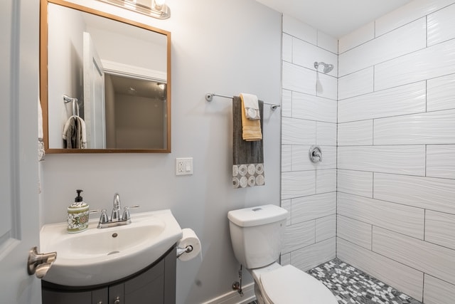 bathroom with a tile shower, vanity, and toilet