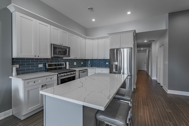 kitchen featuring a breakfast bar, dark hardwood / wood-style floors, white cabinets, appliances with stainless steel finishes, and a center island