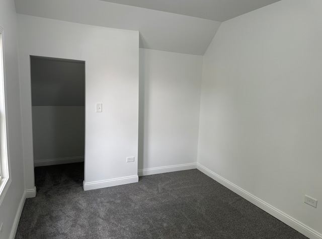 empty room featuring vaulted ceiling and dark colored carpet