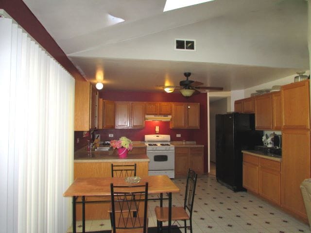 kitchen with sink, white gas range oven, ceiling fan, lofted ceiling with skylight, and black refrigerator