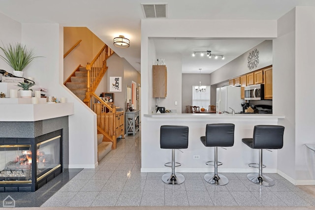 kitchen with a multi sided fireplace, a breakfast bar, decorative light fixtures, and white fridge with ice dispenser